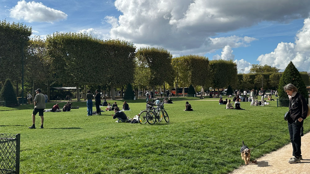 エッフェル塔の麓にあるシャンドマルス公園。天気の良い日に芝生の上でピクニックやおしゃべりをして過ごす人々。