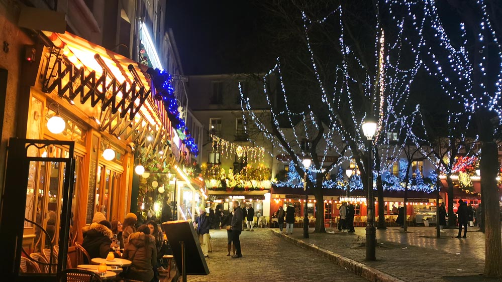 パリのモンマルトルにあるテルトル広場。昼間とは違った雰囲気を見せるクリスマスシーズンの夜の広場。イルミネーションと暖かいオレンジの灯り、レストランのクリスマスデコレーションが可愛い。