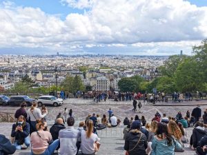 モンマルトルの丘からのパリの眺め。遠くのモニュメントまでよく見える。階段に座って景色を楽しむ若者。